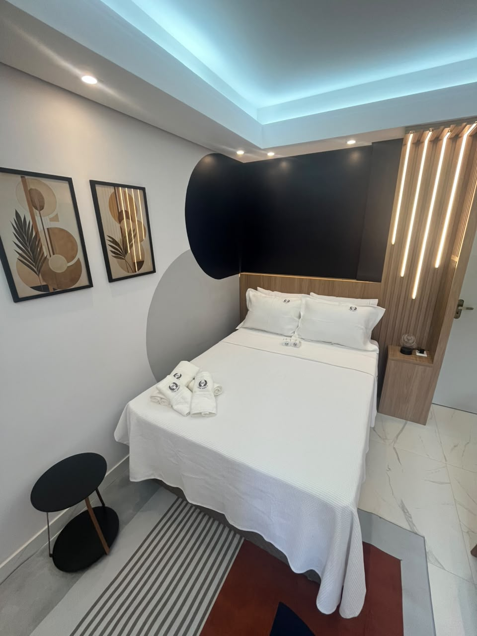 Cama de casal da Suíte Horto II com painel ripado iluminado e enxoval branco