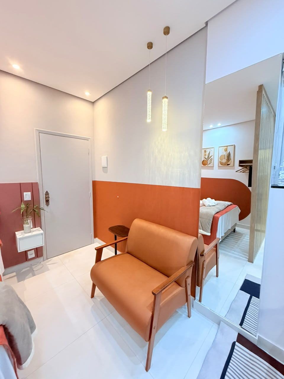 Sala de estar da Suíte Horto III com poltrona terracota, pendentes e cama ao fundo