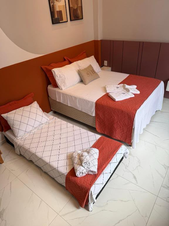 Suíte Horto IV com cama de casal e cama de solteiro extra, enxoval branco com detalhes terracota e toalhas com monograma SH